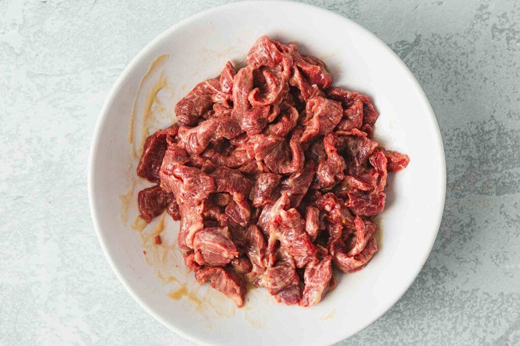 Raw steak pieces in a white bowl.