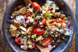 An overhead view of the mixed Greek chicken salad in a mixing bowl with wood salad tongs.