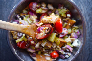 An overhead view of a wooden spoon lifting a bit of Greek chicken salad out of a mixing bowl.