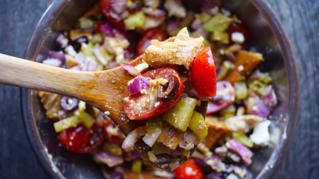 And overhead view of a wooden spoon lifting a bit of Greek chicken salad out of a mixing bowl.