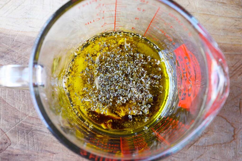 A measuring cup holding the Greek Chicken Salad dressing ingredients.