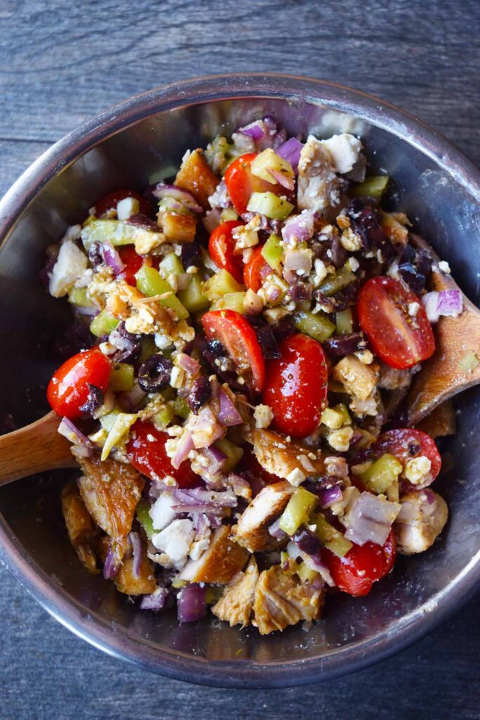 An overhead view of a metal mixing bowl filled with Greek chicken salad.