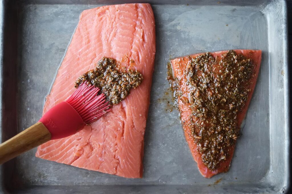 Oil and herb mix being brushed on the salmon fillets with a basting brush.