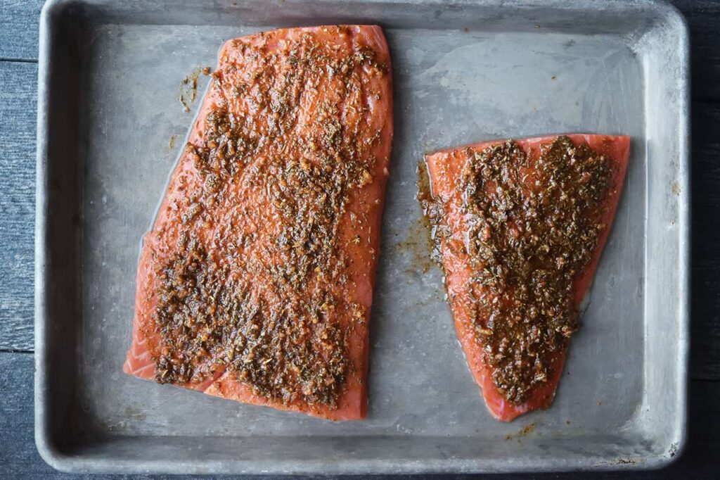 Salmon fillets covered in herb mixture on a baking sheet.