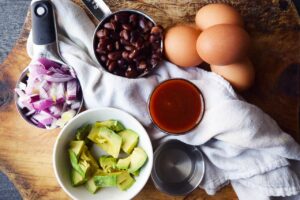 Mexican Scrambled Eggs recipe ingredients gathered on a wood cutting board in individual containers.