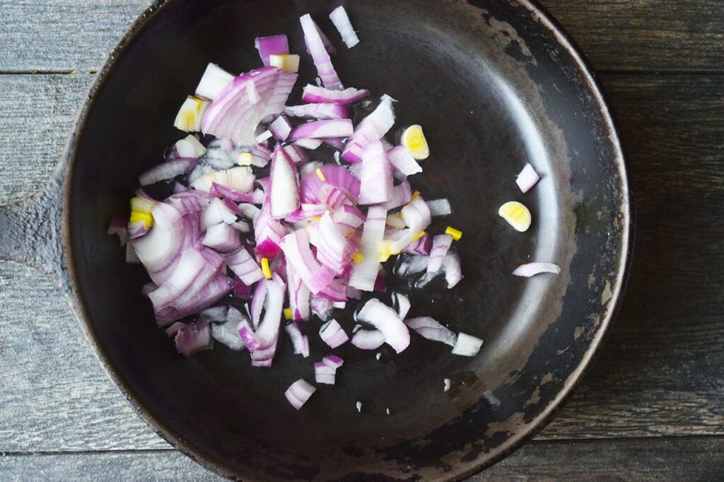 Raw, chopped onions in a black skillet with oil.