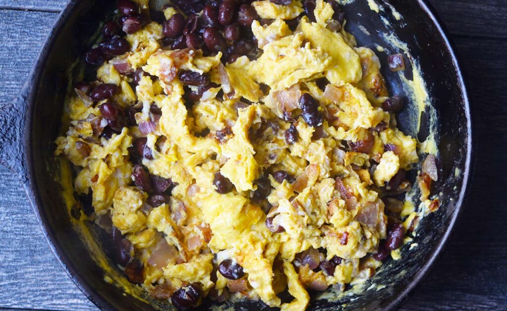 Black beans added to scrambled eggs in a black skillet.