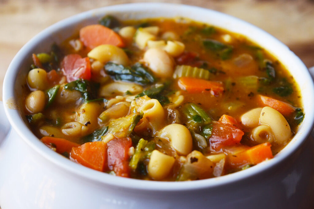 A side view of a white crock filled with Pasta Fagioli.