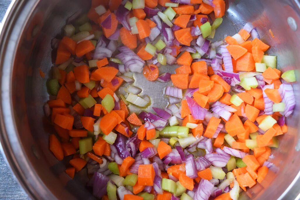 Raw, chopped, carrots, onions, and celery cooking in oil in a large soup pot.