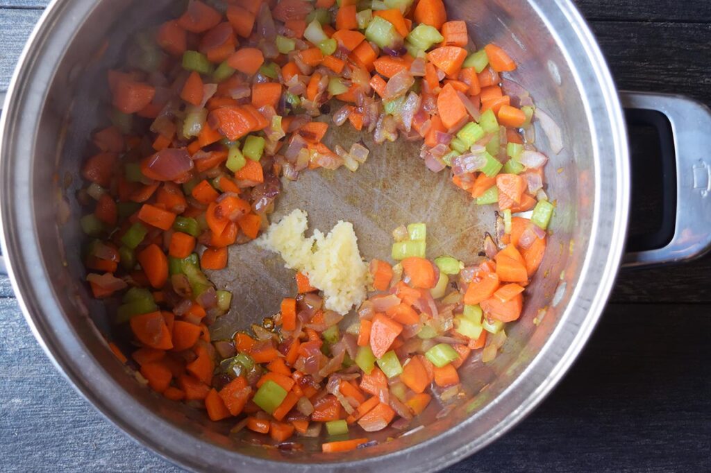 Raw garlic added to saut&eacute;d veggies in a soup pot.