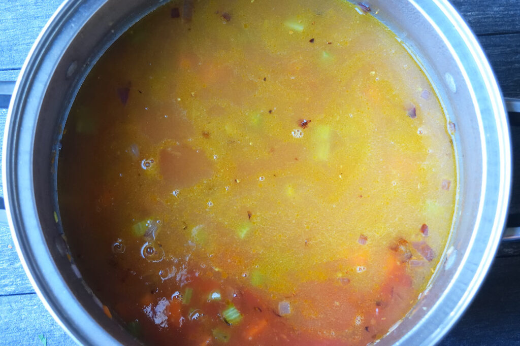 Broth and diced tomatoes added to veggies in a soup pot.