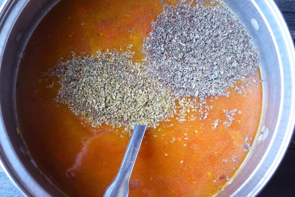 Spices added to the broth and veggies in a soup pot.