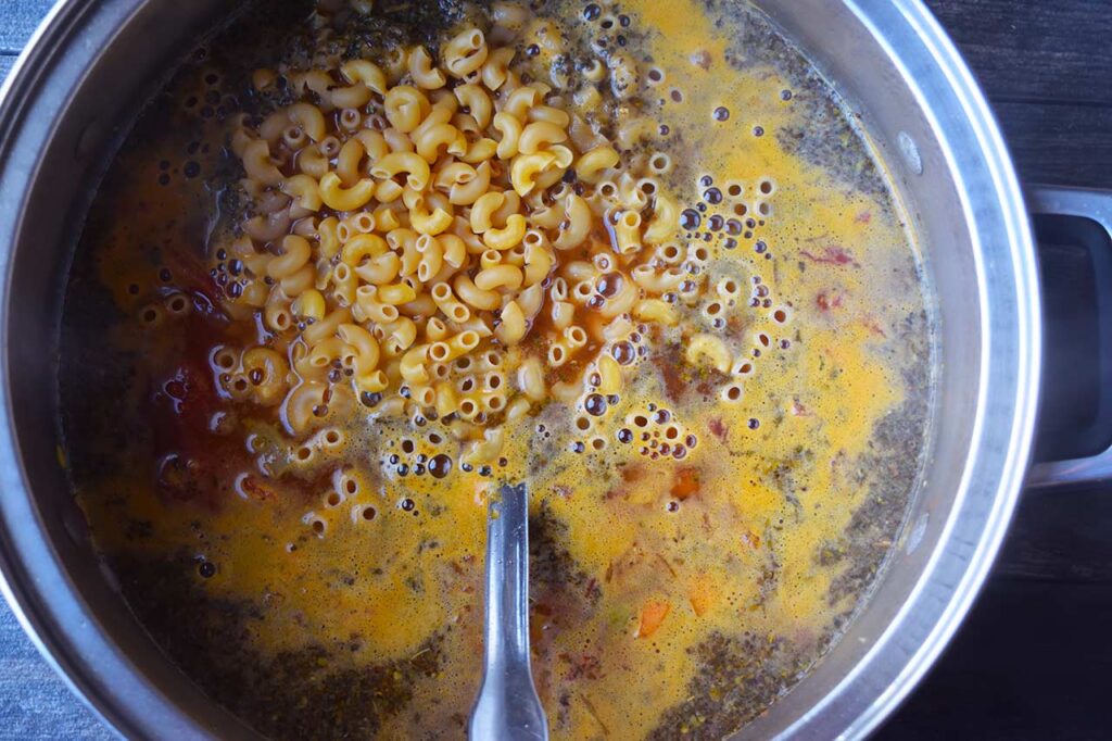 Raw pasta added to broth and veggies in a soup pot.