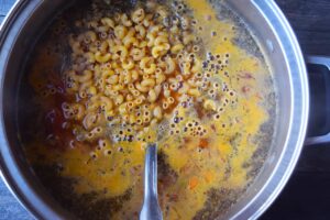 Raw pasta added to broth and veggies in a soup pot.