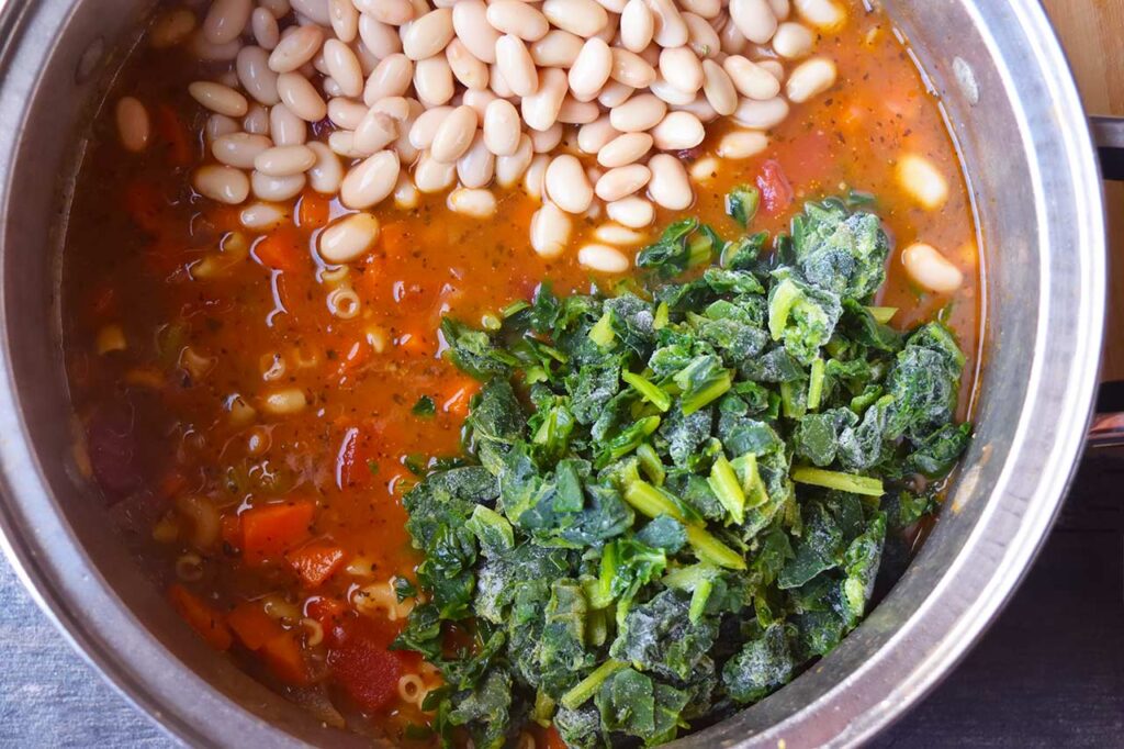 Beans and frozen spinach added to a soup pot of Pasta Fagioli.