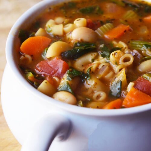 A side view of a white crock filled with Pasta Fagioli.