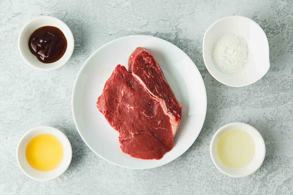 Raw beef and ingredients in individual, white bowls.