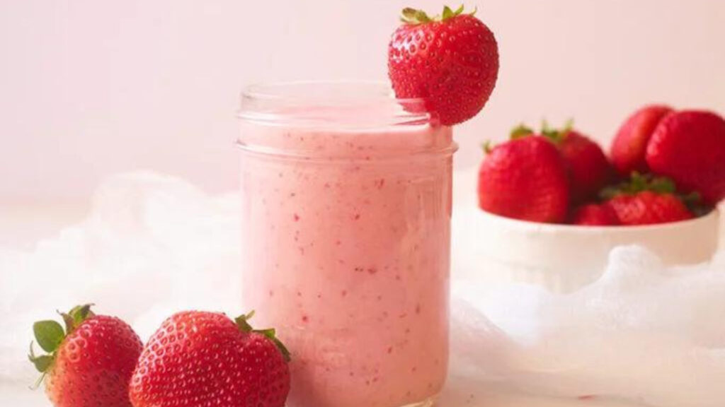 A small, glass jar filled with Strawberry Smoothie and garnished with a fresh strawberry.