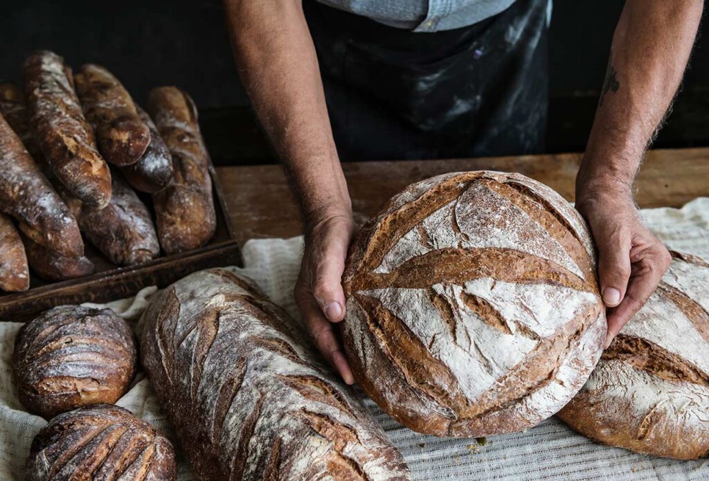 Hands holding a loaf of bread, surrounded by other loaves of bread.