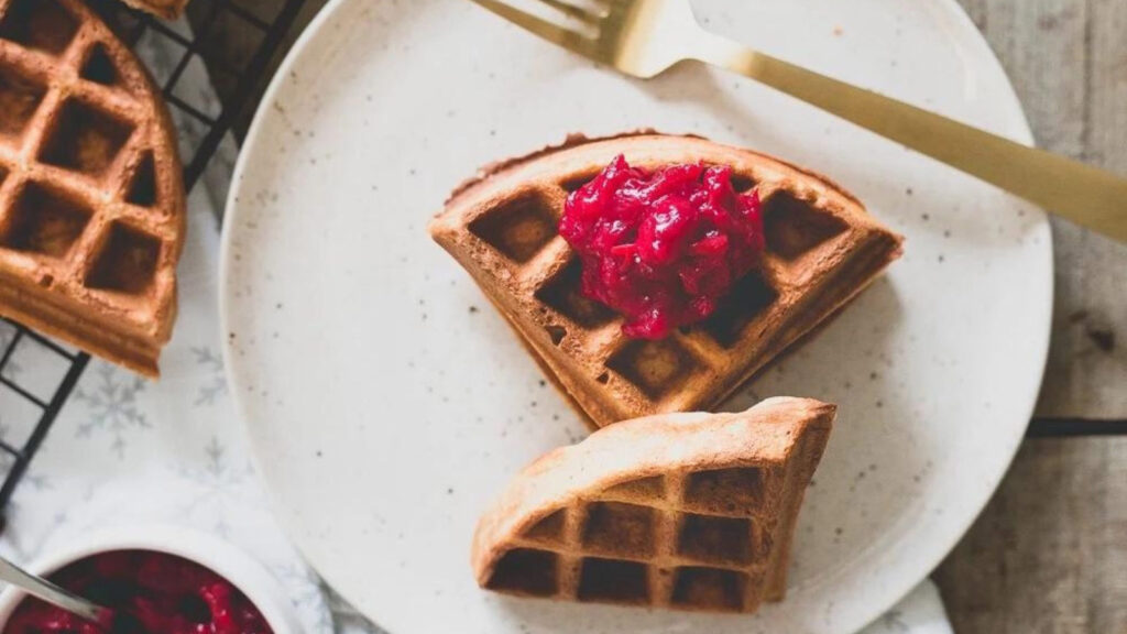 Chestnut flour waffle quarters on a plate with compote on one quarter.
