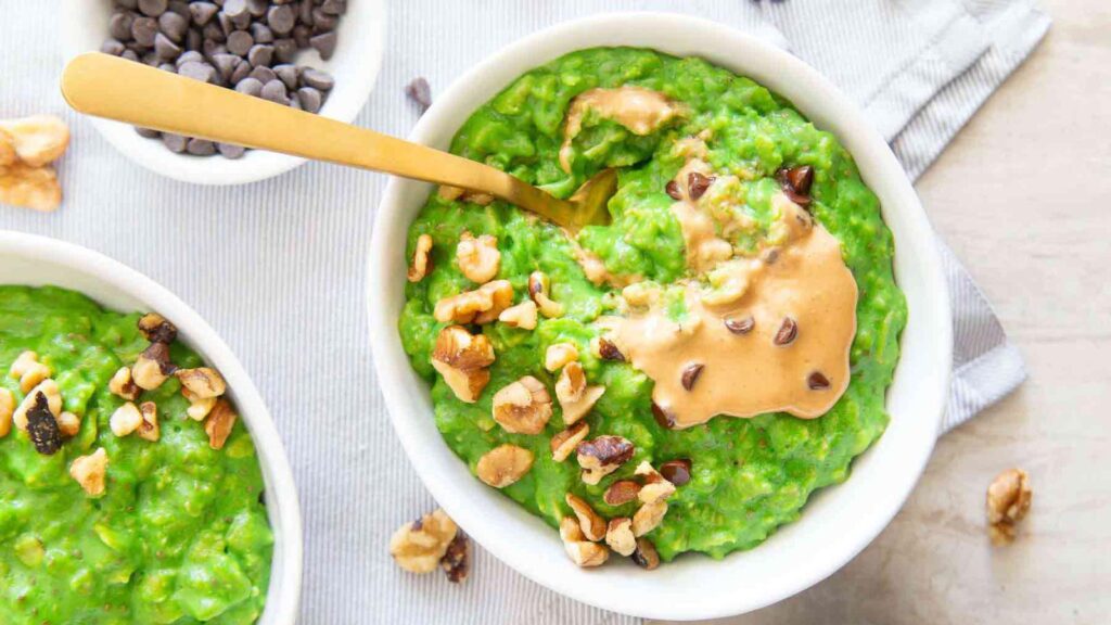 Two white bowls filled with green oatmeal, topped with peanut butter and chopped walnuts.
