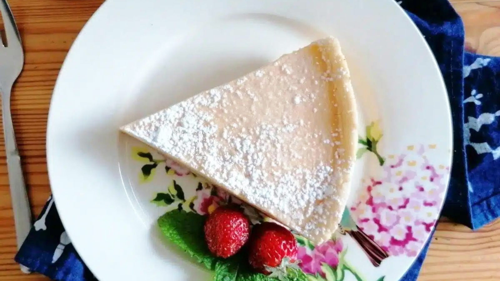 An overhead view of a slice of milk pie on a white plate with two strawberries.