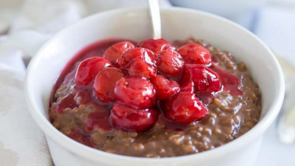 A white bowl filled with chocolate oats and topped with cherries.