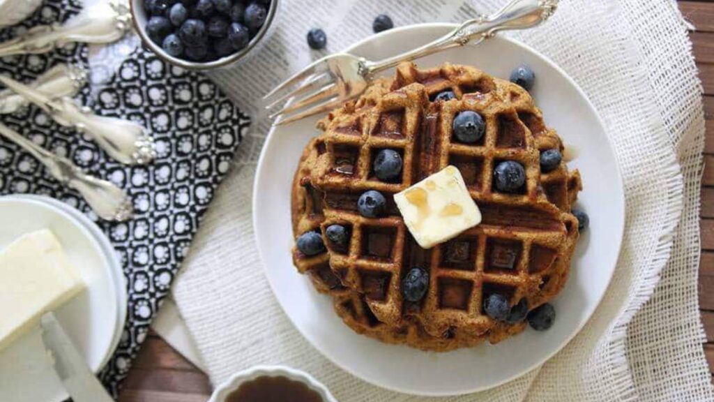 An overhead view of a plate of sweet potato waffles with fresh blueberries and a pat of butter.