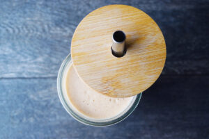 A lid sitting to the side of a glass with a peak into the glass filled with Almond Butter Almond Milk.
