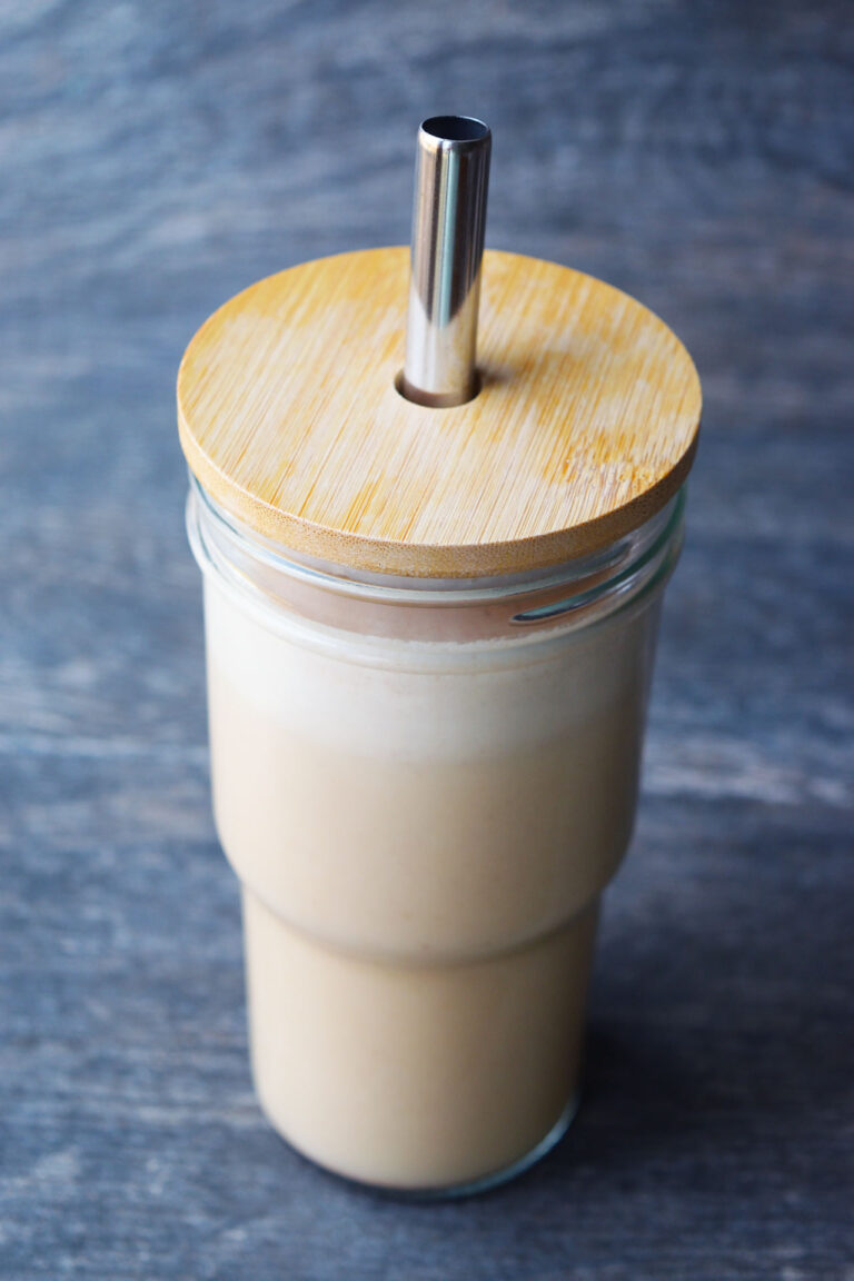A side view of a glass with wood lid and metal straw filled with Almond Butter Almond Milk.