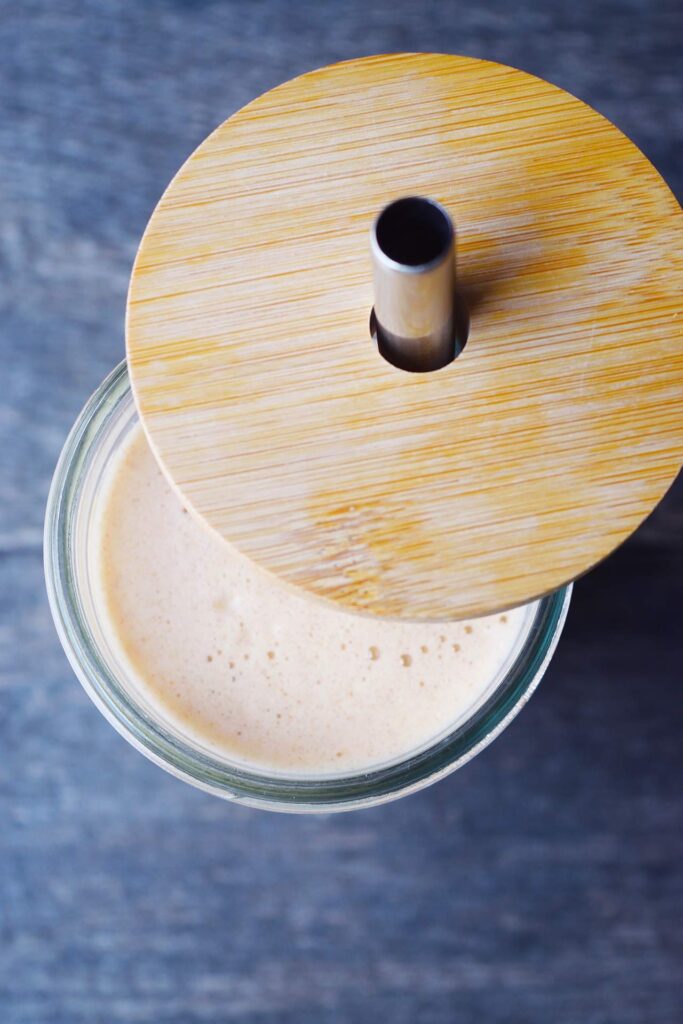 An overhead view of a lid partially removed from a glass to show the Almond Butter Almond Milk inside.