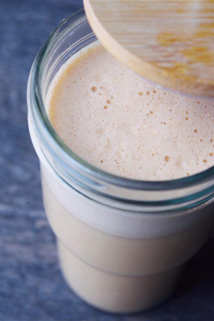 A side view of a glass with the lid partially removed, filled with Almond Butter Almond Milk.