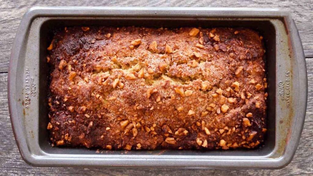 A loaf pan with a loaf of apple bread in it.