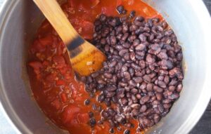 Black beans added to soup in a large pot.