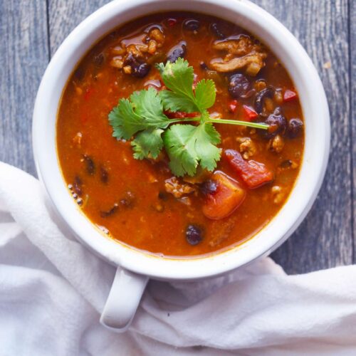 An overhead view of a white crock filled with Black Bean Taco Soup. A white towel lays next to the bowl.