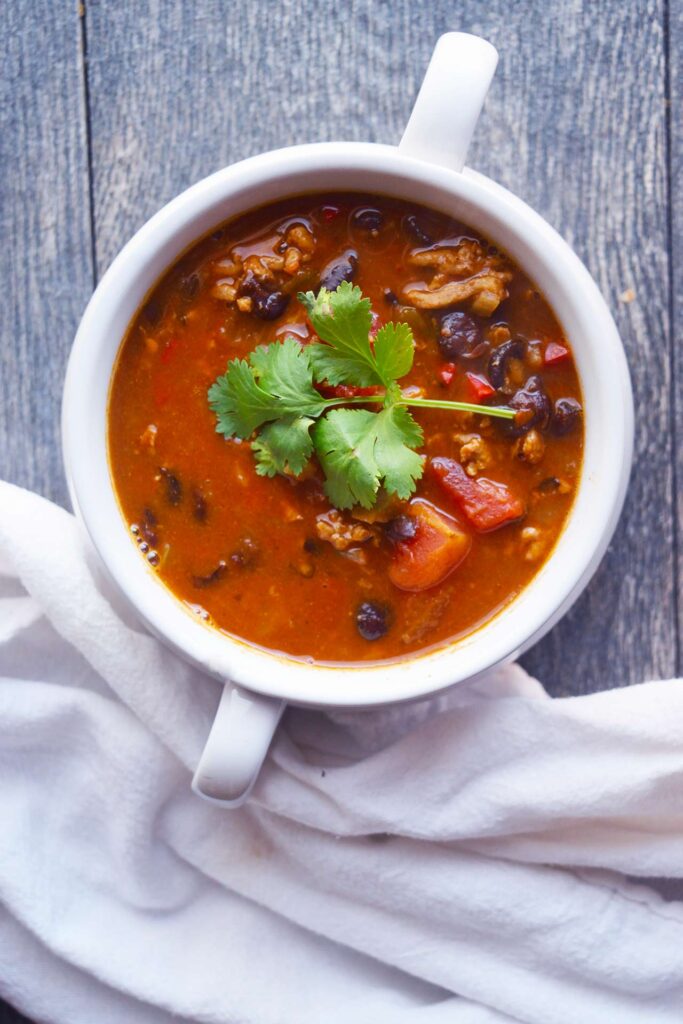 An overhead view of a white crock filled with Black Bean Taco Soup. A white towel lays next to the bowl.