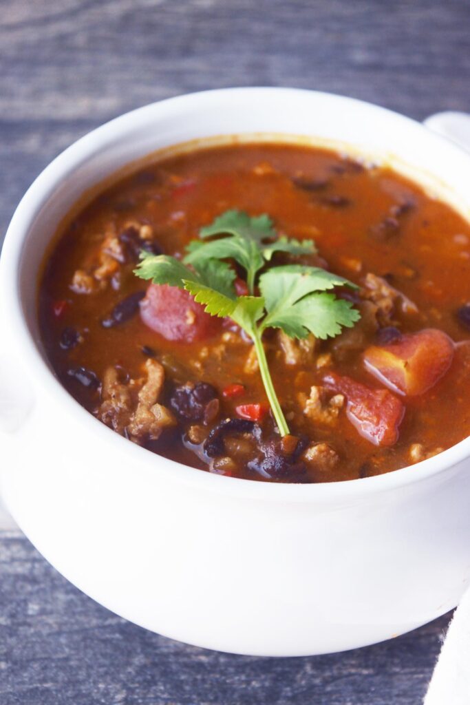 A side view of a whit crock filled with Black Bean Taco Soup and garnished with a twig of fresh cilantro.