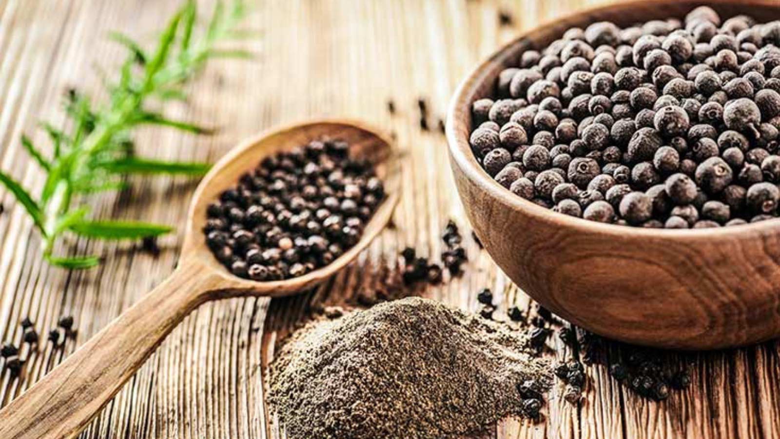 A bowl and spoon lay on a table, both filled with black pepper corns.