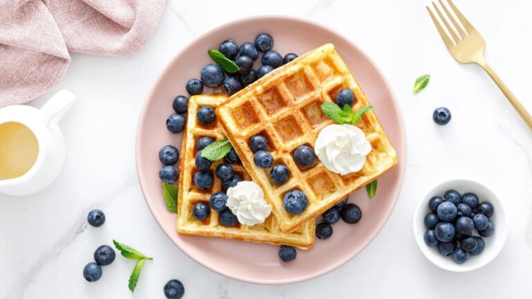 An overhead view of two lupin flour waffles on a plate with fresh blueberries and a dollop of whipped cream.
