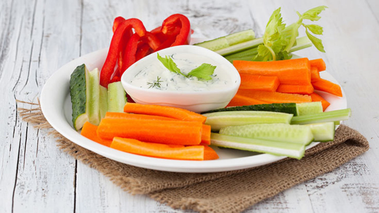 A white plate of vegetable sticks with a small white bowl of dip in the middle.