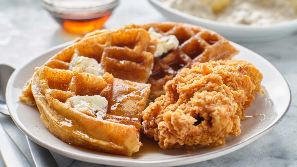 A waffle cut in half with a piece of fried chicken next to it.