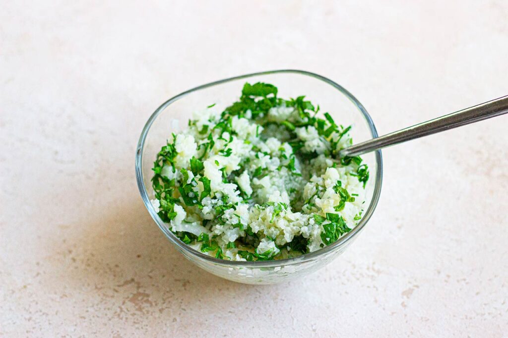 A bowl holds cauliflower rice mixed with lemon juice and chopped parsley.