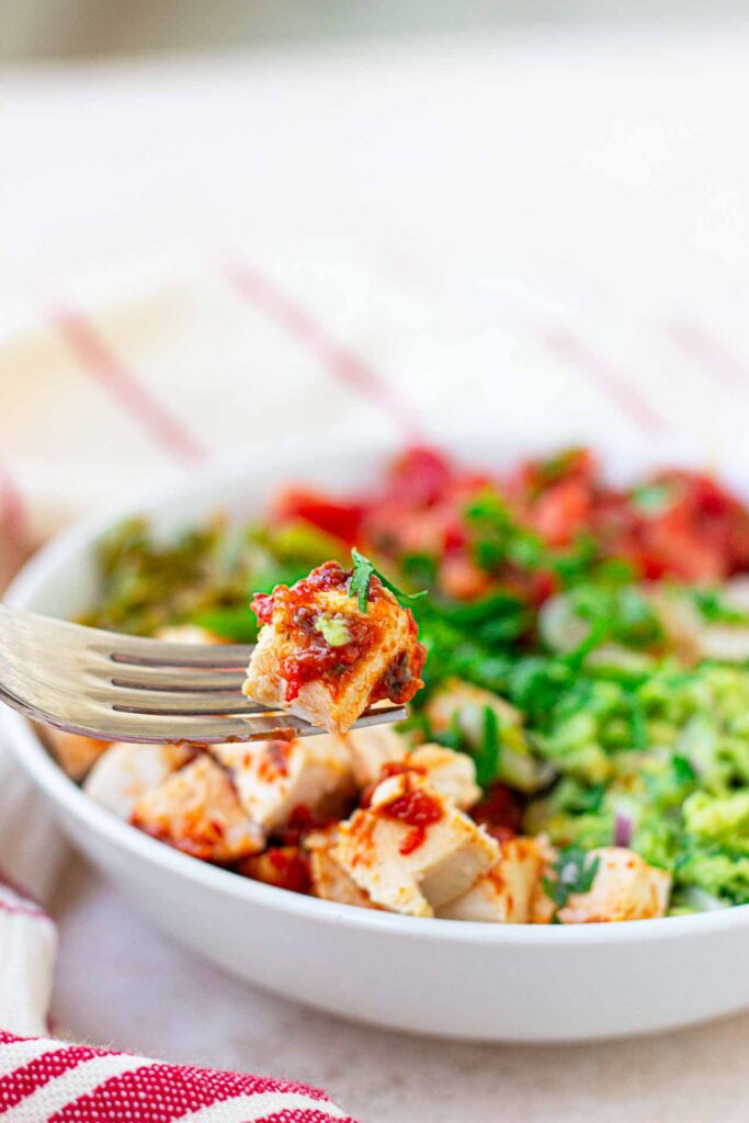 A fork lifts up a piece of chicken from a bowl filled with Avocado Chicken Salad.