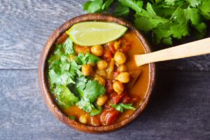 An overhead view of a wood bowl filled with Chickpea Curry and garnished with fresh cilantro and a lime wedge.