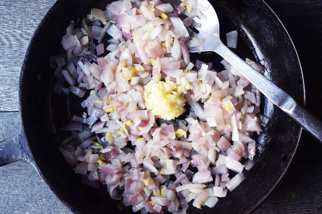 A skillet with sautéd onions and fresh, pressed garlic just added to the middle of the pan.