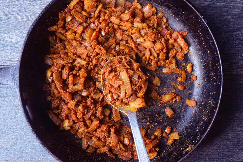 Sautéd onions, ginger, and garlic coated in spices in a black skillet.