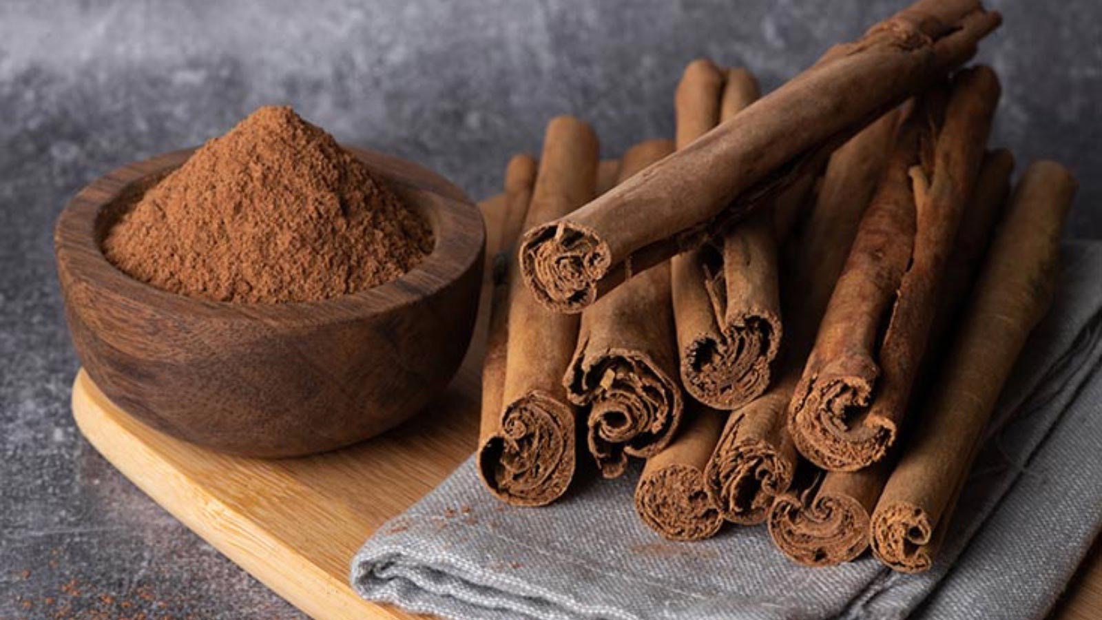 Cinnamon sticks and a small wood bowl of ground cinnamon on a cutting board.