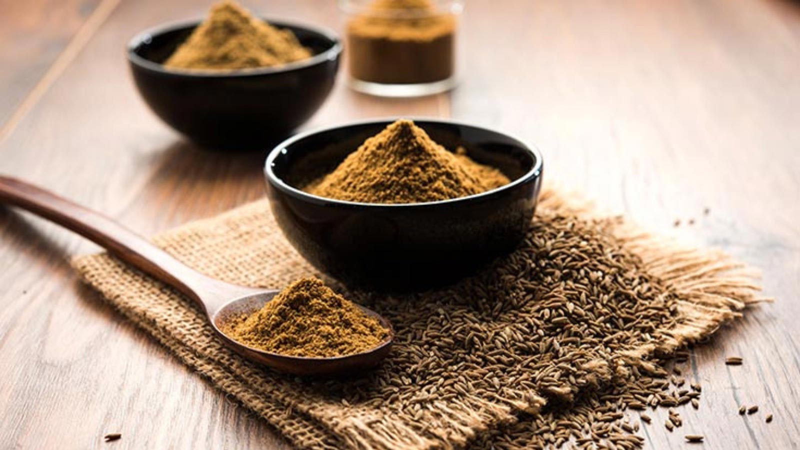 Ground cumin in small bowls and on a wood spoon.