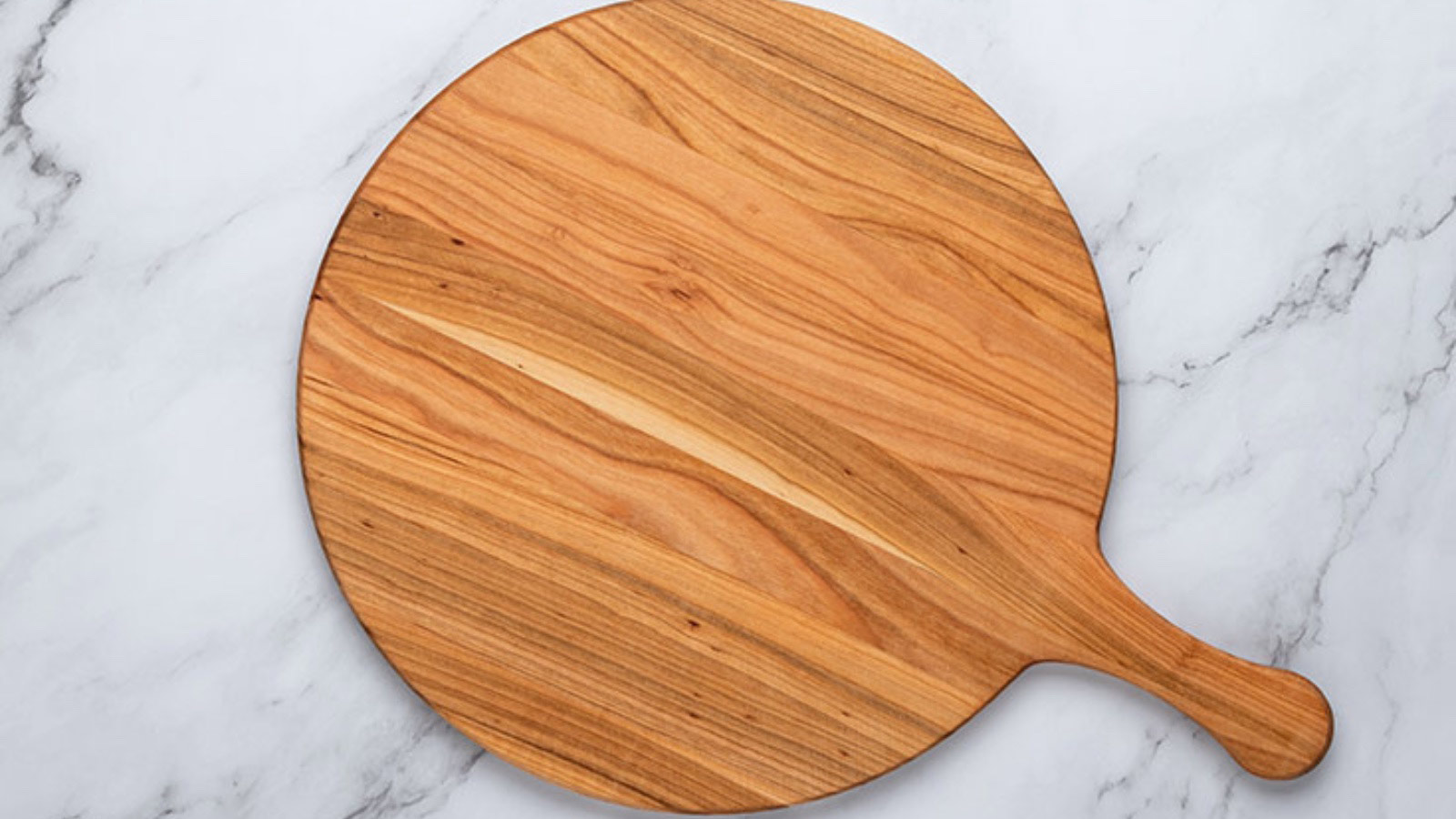 A round cutting board with a handle on a marble surface.