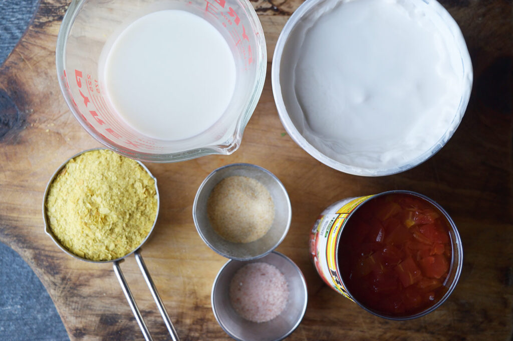 Ingredients for vegan queso in individual containers on a wood cutting board.